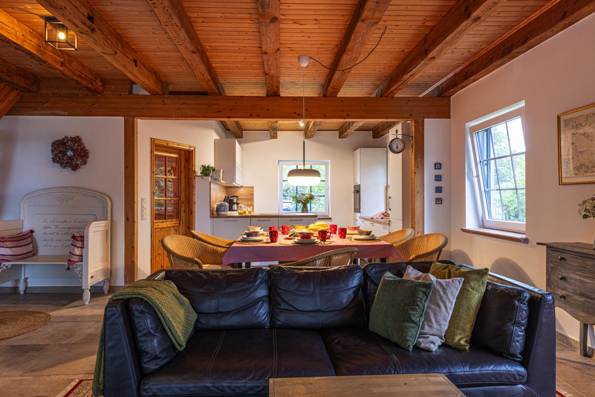 Ferienhaus Remise — Charmantes Landhausgefühl mit Holzbalkendecken und blauem Fensterladen.