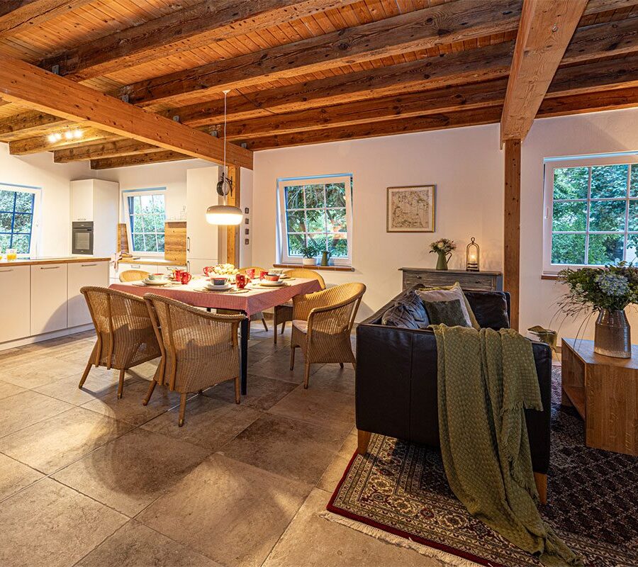 Ferienhaus Remise — Charmantes Landhausgefühl mit Holzbalkendecken und blauem Fensterladen.